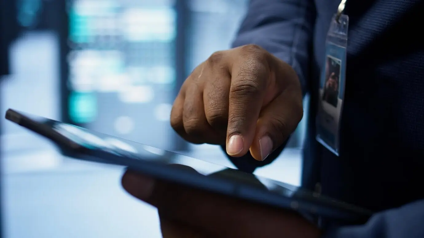 Close-up of a man using a tablet in a data center, verifying that the rigs are functioning.